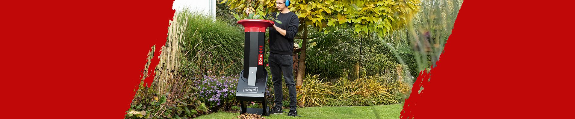 Ein Mann steht in einem Garten und bedient einen Scheppach-Gartenhäcksler. Im Hintergrund sind verschiedene Pflanzen und ein Rasenbereich zu sehen.