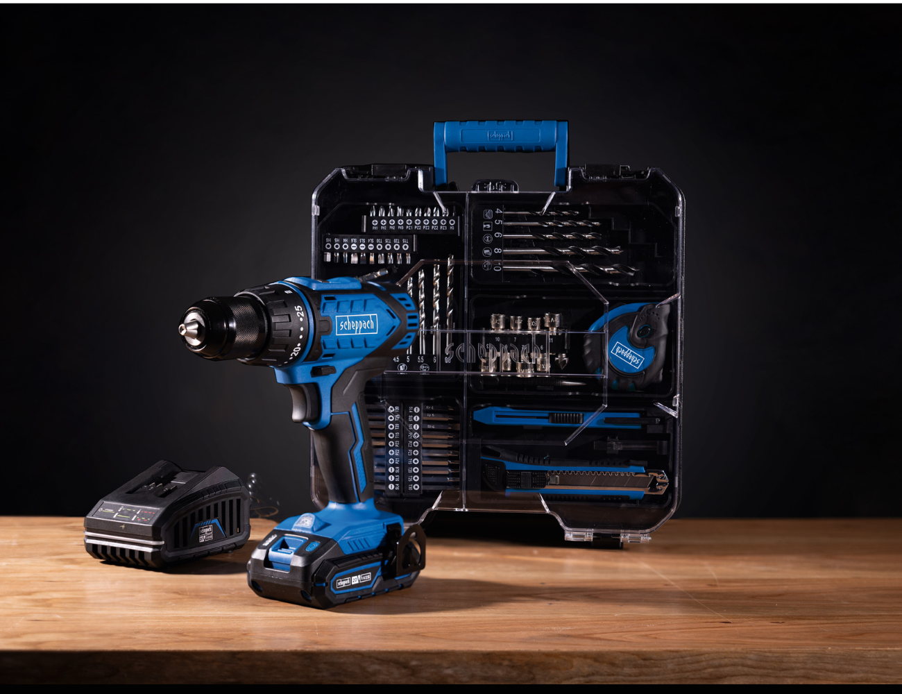 Scheppach 20V Akku-Bohrschrauber mit Akku und Ladegerät. Im Hintergrund ein Werkzeugkoffer mit verschiedenen Zubehörteilen.