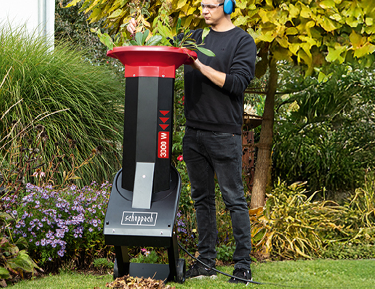 Ein Mann bedient einen Scheppach-Gartenhäcksler im Garten. Der Häcksler hat eine Leistung von 3000 Watt.