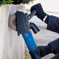 Scheppach Messingdrahtbürste MRS1300 im Einsatz an einer Wand. Die Bürste ist an einem Winkelschleifer befestigt und wird von einer Person mit Handschuhen gehalten.