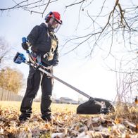 Mann mit Akku-Freischneider beim Einsatz im Garten, mit Sicherheitsausrüstung und Werkzeug