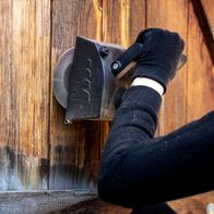 Scheppach Schleiflamellenbürste im Einsatz an einer Holzoberfläche. Die Bürste wird von einer Hand mit Handschuh gehalten und bearbeitet eine Holzwand.