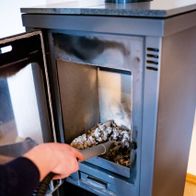 Der Aschesauger AVC20 von Scheppach im Einsatz, Asche wird in den Behälter gesaugt. Ein Handschuh wird zum Schutz getragen.