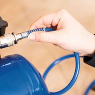 A craftsman is screwing a hose onto the Scheppach Compressor HC06. The compressor has a 6-litre tank capacity and a power of 1200 watts.