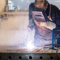 Ein Arbeiter schweißt mit dem Schweißgerät Fülldraht WSE5000-Multi von Scheppach. Das Gerät liegt auf einem Metalltisch und zeigt 84% und 269° an.