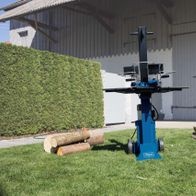 Holzspalter HL730 von Scheppach im Freien mit Holzstapeln daneben. Im Hintergrund ein Gebäude mit geschlossener Tür.