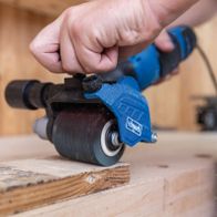 Scheppach-Bürstenschleifer mit rotem und schwarzen Gehäuse, Detailansicht eines Schleifbürstenaufsatzes auf Holzwerkstück