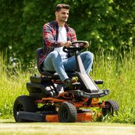 Mann sitzt auf Akku-Aufsitzrasenmäher mit 12-stufiger Schnitthöhenverstellung und zeigt entspanntes Lächeln.