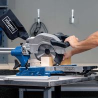 Kappzugsäge HM110MP von Scheppach im Einsatz. Ein Benutzer bedient die Säge an einem Werkstück. Die Säge ist auf einem Tisch montiert und wird von einem Benutzer mit beiden Händen gehalten.