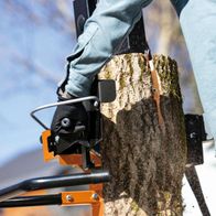 Der Meterholzspalter IX-CLS-10t IXES von Scheppach zeigt einen Baumstumpf, der von der Maschine gespalten wird. Die Maschine verfügt über eine robuste Halterung und eine scharfe Klinge zum effizienten Spalten von Holz.