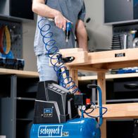 Scheppach HC30ox compressor in use. A man is using an air staple gun on a wooden board. The compressor has a 24-litre tank and a power of 1.5 HP.