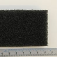 Ein schwarzer Schwammfilter vor einem Lineal. Der Filter ist etwa 10 cm breit und 6 cm hoch.
