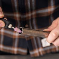 Ein Doppelschleifer mit flexibler Welle wird mit einem Schleifaufsatz verbunden. Die Hände halten den Schleifaufsatz und den Schleifer fest. Der Hintergrund ist unscharf und zeigt ein gemustertes Tuch.