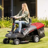 Aufsitzrasenmäher MR224-61 von Scheppach mit 6.8PS, 61cm Schnittbreite, 150L Fangsack und Elektro-Start. Die Frau sitzt auf dem Rasenmäher und steuert ihn auf einem Rasen.