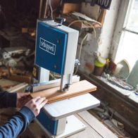 Eine Person bedient eine Bandsäge HBS20 von Scheppach. Die Maschine ist in Betrieb und schneidet Holz. Die Person trägt Schutzbrille und arbeitet konzentriert.