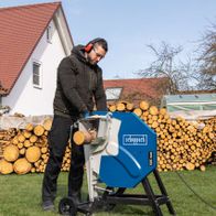 Ein Mann bedient die Wippsäge HS510 von Scheppach im Freien. Im Hintergrund sind Holzstapel zu sehen.