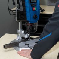 Tischbohrmaschine DP60 Scheppach mit digitaler Anzeige und Laserführung. Ein Benutzer bedient die Maschine, die auf einem Metallstück arbeitet.