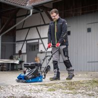 Mann mit Schutzausrüstung betreibt Scheppach-Gräsmaschine mit Handsteuerung