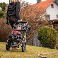 Benzin Hochdruckreiniger HCP2600 Scheppach, seitliche Ansicht, Person schiebt Gerät auf Rasenfläche.