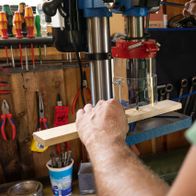The Scheppach bench drill DP19Vario in use. A wooden board is clamped on the worktable and being drilled.