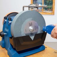 Scheppach Wet Bench Grinder Tiger 7000S in use. A user holds an object against the grinding wheel. The grinding wheel is 250mm in diameter with a grit of 220.