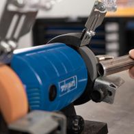 Ein Handwerker hält einen Metallrohrstab in einen Doppelschleifer von Scheppach. Der Schleifer ist eingeschaltet und bearbeitet das Metallrohr.