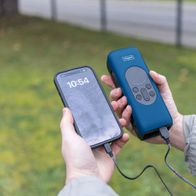 Hände halten ein Smartphone und ein Scheppach-Ladegerät. Das Smartphone zeigt 10:54 Uhr an und ist mit dem Ladegerät verbunden.
