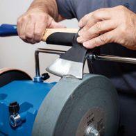 Ein Mann schärft ein Beil mit dem Nass-Schleifsystem TIGER 7000S von Scheppach. Der Schleifstein ist in Betrieb und das Beil wird von Hand geführt.