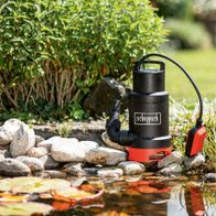 Scheppach Schmutzwassertauchpumpe SWP800-2 im Einsatz an einem Gartenteich mit Steinen und Pflanzen im Hintergrund.