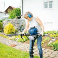 Frau nutzt Scheppach-Erdbohrer für Gartenarbeit, Bohrgerät mit Bohraufsatz im Einsatz