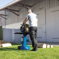 Ein Mann bedient den Holzspalter HL810 von Scheppach im Freien. Im Hintergrund sind ein Schuppen und ein Holzstapel zu sehen.