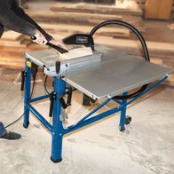 Tischkreissäge HS120o von Scheppach im Einsatz. Ein Benutzer führt ein Brett durch die Säge. Die Säge ist auf einem blauen Ständer montiert und hat eine Tischverlängerung.