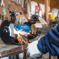 Ein Scheppach-Werkzeug wird in einer Werkstatt verwendet. Funken fliegen beim Arbeiten mit dem Gerät. Im Hintergrund hängen verschiedene Werkzeuge an der Wand.