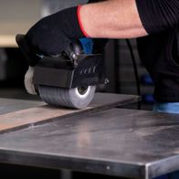 Scheppach Siliziumkarbidbürste im Einsatz an einer MRS1300 Satiniermaschine. Die Bürste wird von einem Nutzer geführt und bearbeitet eine Metallplatte.