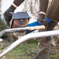 Scheppach Schleifstreifenbürste im Einsatz an einer MRS1300 Satiniermaschine. Die Bürste wird von einem Nutzer mit Handschuhen gehalten und bearbeitet Metall.