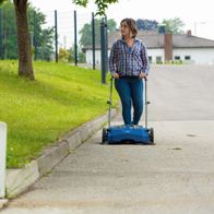 Person mit Handkurbel und Scheppach-Kehrmaschine auf dem Weg