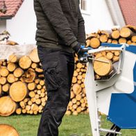 Wippsäge HS510 von Scheppach im Einsatz, Holzscheite werden zerkleinert. Im Hintergrund ein Holzstapel.