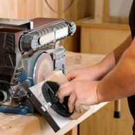 Band- und Tellerschleifer BTS900 Scheppach im Einsatz. Ein Nutzer schleift ein Holzstück mit dem Tellerschleifer. Die Maschine ist auf einem Holztisch platziert.