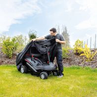 Ein Mann deckt den Scheppach Aufsitzrasenmäher MR224-61 ab. Der Rasenmäher steht auf einem grünen Rasen.