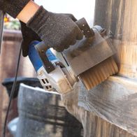 Scheppach Schleifstreifenbürste im Einsatz an der MRS1300 Satiniermaschine. Die Bürste wird von einer Hand in Arbeitshandschuhen gehalten und bearbeitet eine Holzoberfläche.