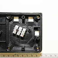 Kabelbox Abdeckung von Scheppach, Ansicht von oben. Die Abdeckung ist rechteckig mit vier Befestigungslöchern an den Ecken und einem zentralen Bereich mit elektronischen Komponenten. Die Maße betragen etwa 9 cm x 7 cm.