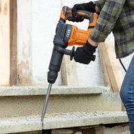 Der Scheppach Elektro-Abbruchhammer IX-DB1500 IXES mit orange-schwarzem Design und schwarzem Griff. Der Hammer wird von einem Arbeiter mit Handschuhen bedient und in eine Betonwand geschlagen.