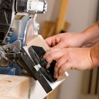 Ein Benutzer bedient den Scheppach Band- und Tellerschleifer BTS900, während er ein Holzstück schleift. Die Hände führen das Holz vorsichtig über die Schleifscheibe.