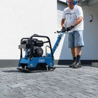 Mann betreibt eine Scheppach-Rüttelplatte mit Fahrvorrichtung auf einer Pflasterfläche