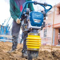 Der Scheppach Vibrationsstampfer VS1000 mit 5.6 PS und 10000J. Der Stampfer hat eine gelbe Federung und wird im Einsatz gezeigt.