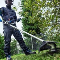 Person beim Einsatz eines Akku-Freischneiders mit Halterung und Schneidwerkzeug für Rasenpflege