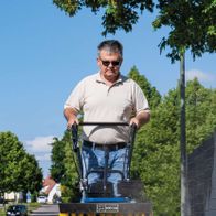 Ein Mann bedient eine Kehrmaschine SC2400p von Scheppach auf einem Gehweg. Die Maschine hat eine Arbeitsbreite von 600 mm.