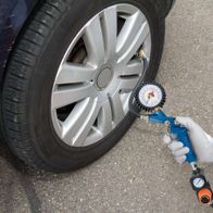 Ein Scheppach-Kompressor wird verwendet, um den Reifendruck eines Autos zu überprüfen. Der Kompressor ist mit einem Druckmesser ausgestattet und wird von einer Person mit Handschuhen bedient.