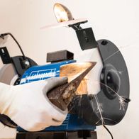 Scheppach Doppelschleifer BG200AL im Einsatz, Hand führt Schleifscheibe. Produktansicht von vorne.