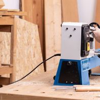 Scheppach Drechselmaschine DM1100T im Einsatz. Ein Benutzer bearbeitet ein Holzstück mit der Maschine. Die Maschine hat eine blaue und weiße Farbgebung und ist auf einem Holztisch montiert.